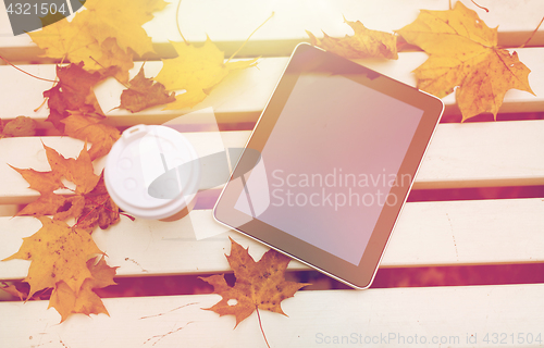 Image of tablet pc and coffee cup on bench in autumn park