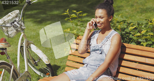 Image of Cheerful woman talking smartphone in park