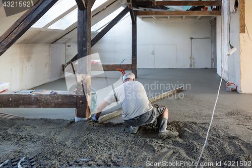 Image of Laborer leveling sand and cement screed over floor heating.