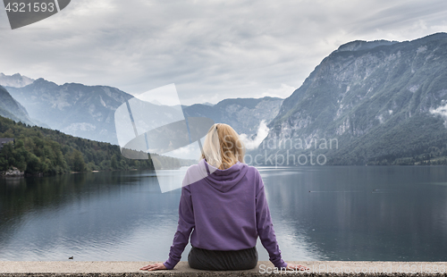 Image of Woman wearing purple hoodie watching tranquil overcast morning scene at lake Bohinj, Alps mountains, Slovenia.