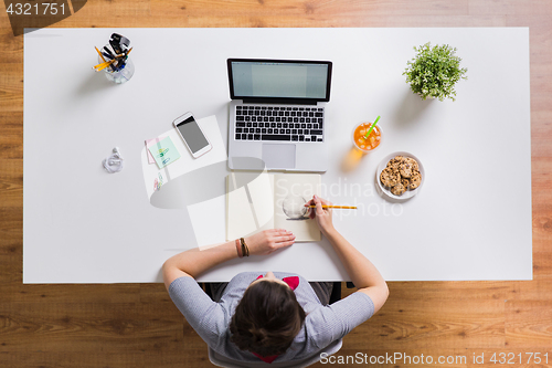 Image of woman with laptop drawing in notebook at office