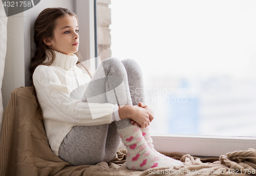 Image of sad girl sitting on sill at home window in winter
