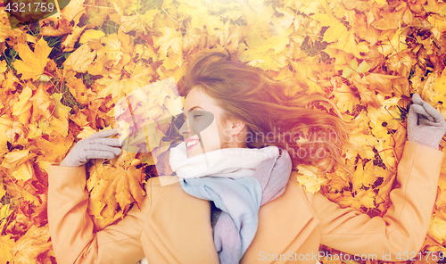 Image of beautiful happy woman lying on autumn leaves