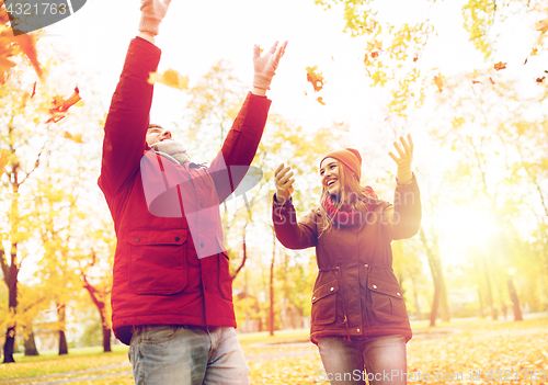 Image of happy young couple throwing autumn leaves in park