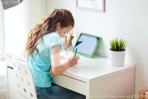 Image of girl with tablet pc writing to notebook at home