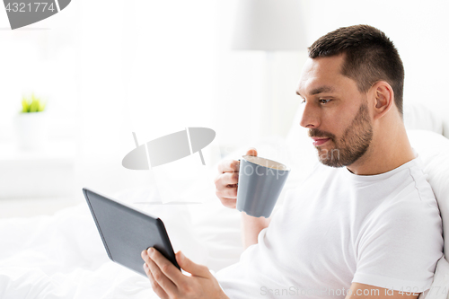 Image of man with tablet pc drinking coffee in bed at home