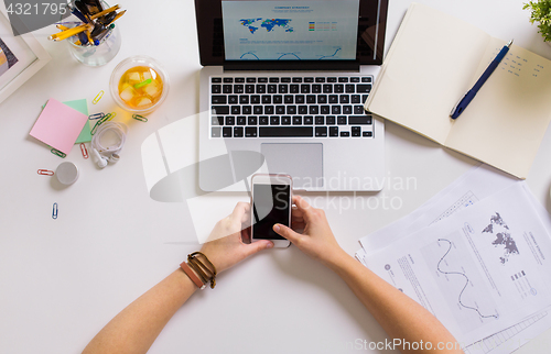 Image of hands with smartphone and laptop at office table