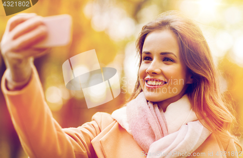 Image of woman taking selfie by smartphone in autumn park