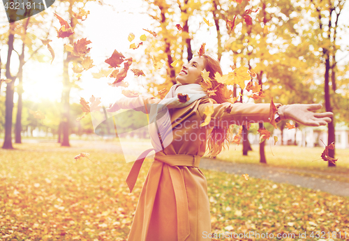 Image of happy woman having fun with leaves in autumn park