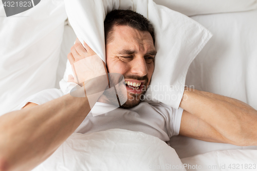 Image of man in bed with pillow suffering from noise