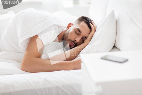 Image of man sleeping in bed with smartphone on nightstand