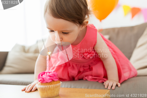 Image of girl blowing to candle on cupcake at birthday