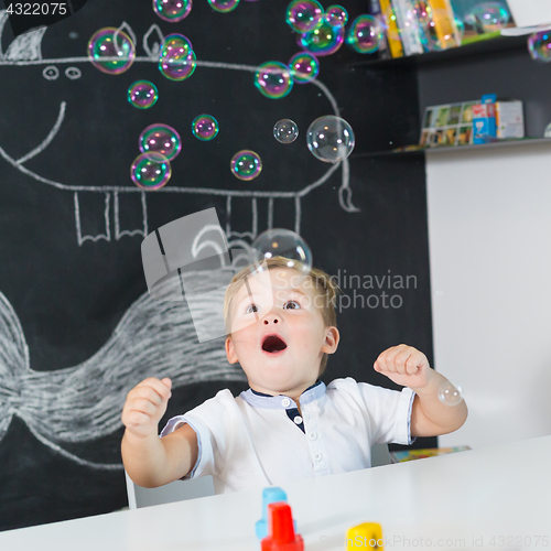 Image of Portrait of cute toddler boy amazed by milky bubbles.