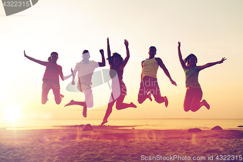 Image of smiling friends dancing and jumping on beach