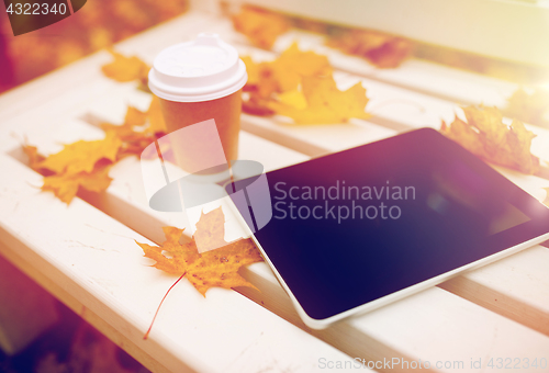 Image of tablet pc and coffee cup on bench in autumn park
