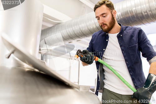 Image of man with hose working at craft beer brewery kettle