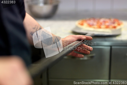Image of cook or baker hand with pizza on peel at pizzeria