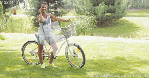 Image of Young cyclist talking phone in park