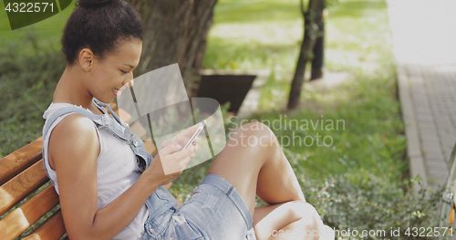 Image of Content girl using smartphone in park