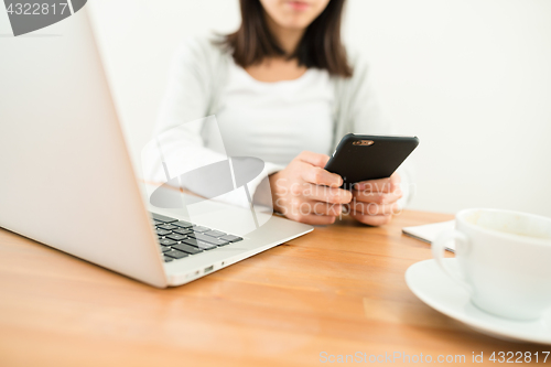 Image of Woman sending sms on cellphone with her laptop computer