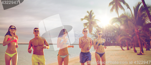 Image of smiling friends in sunglasses running on beach