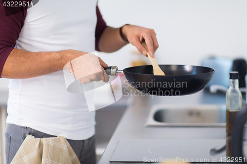 Image of man with frying pan cooking food at home kitchen