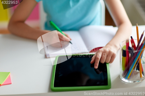 Image of girl with tablet pc writing to notebook at home