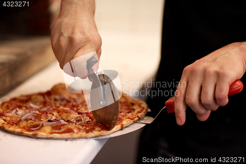 Image of cook hands cutting pizza to pieces at pizzeria