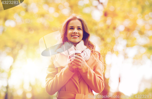 Image of happy young woman drinking coffee in autumn park