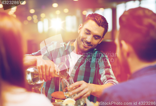 Image of happy man with friends pouring water at restaurant