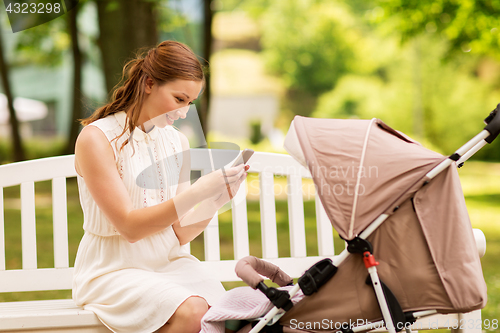 Image of happy mother with smartphone and stroller at park