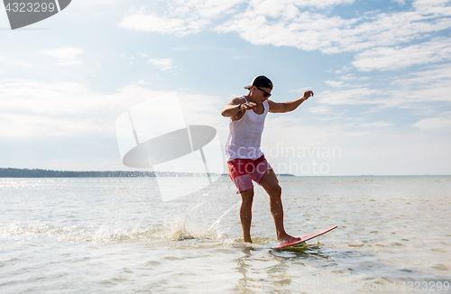 Image of young man riding on skimboard on summer beach