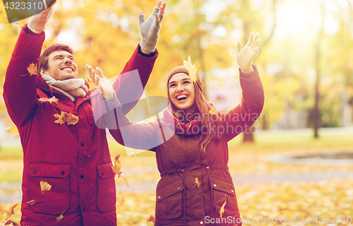 Image of happy young couple throwing autumn leaves in park