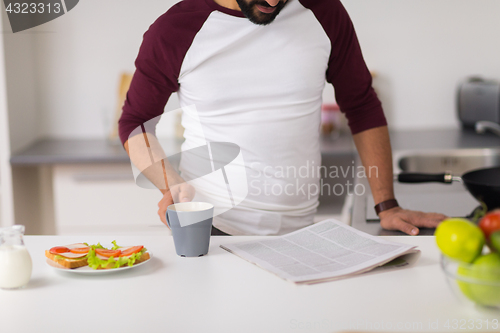 Image of man reading newspaper and eating at home kitchen
