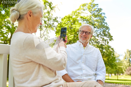 Image of old woman photographing man by smartphone in park