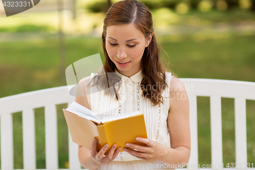 Image of smiling young woman reading book at summer park