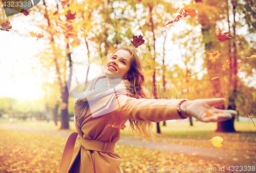 Image of happy woman having fun with leaves in autumn park