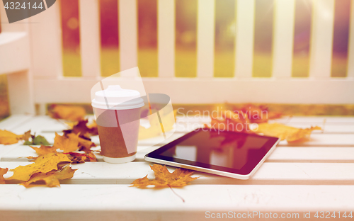 Image of tablet pc and coffee cup on bench in autumn park