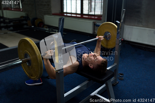 Image of young man flexing muscles with barbell in gym