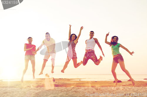 Image of smiling friends dancing and jumping on beach