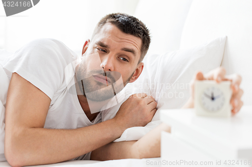 Image of young man in bed reaching for alarm clock