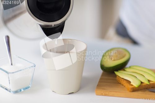 Image of kettle pouring hot water to tea cup at home