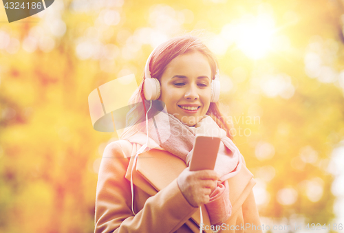 Image of woman with smartphone and earphones in autumn park