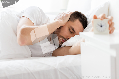 Image of young man in bed reaching for alarm clock