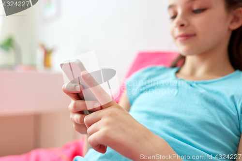 Image of smiling girl texting on smartphone at home