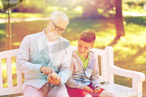 Image of old man and boy with smartphones at summer park