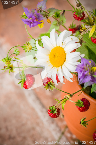Image of Ripe strawberries and a bouquet of forest flowers in a clay mug