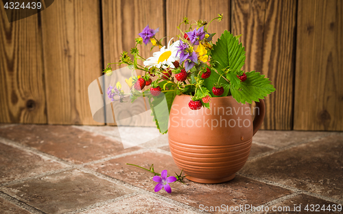 Image of Ripe strawberries and a bouquet of forest flowers in a clay mug