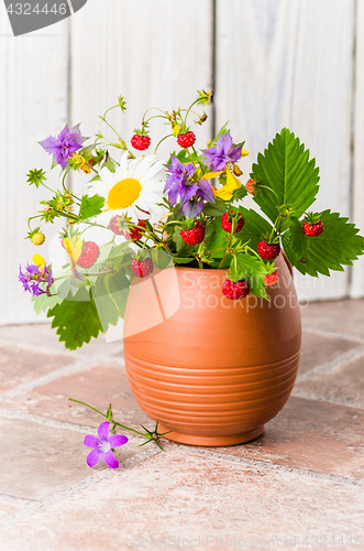 Image of Ripe strawberries and a bouquet of forest flowers in a clay mug