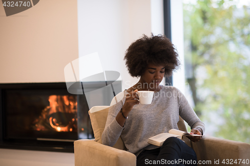 Image of black woman reading book  in front of fireplace